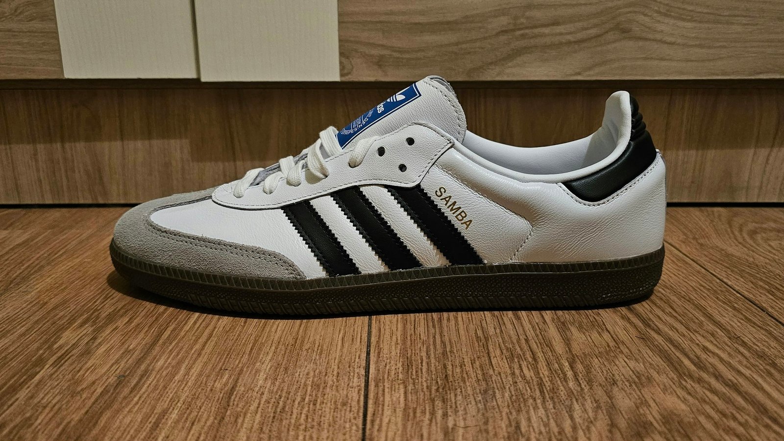 White and black Adidas sneakers on a wooden floor