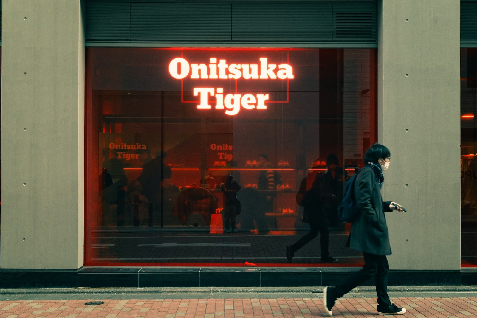 Man walking past a brightly lit Onitsuka Tiger store at night