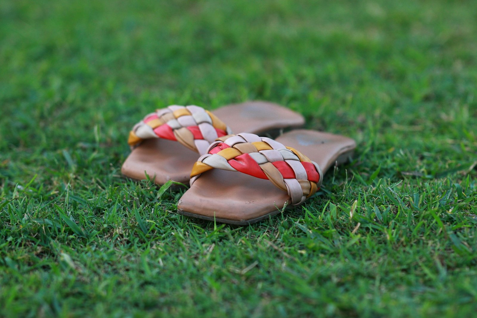 Pair of colourful woven sandals on green grass