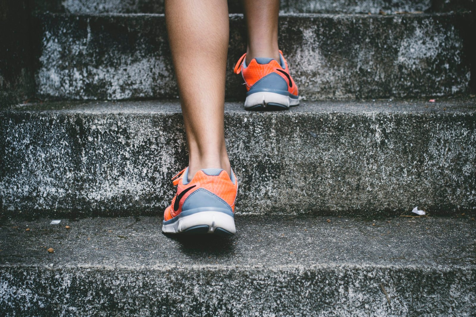 Person in orange and grey sports shoes walking up concrete stairs